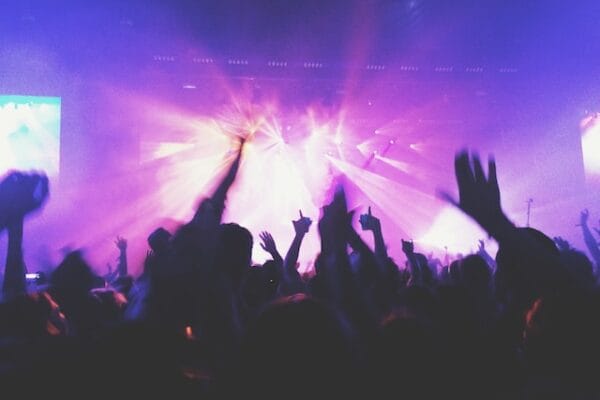 Silhouetted concert crowd with raised hands under purple and pink stage lights
