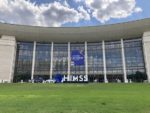 Exterior view of a large curved modern building with glass facade and concrete exterior, showcasing the HIMSS (Healthcare Information and Management Systems Society) logo and signage, representing a major healthcare technology conference or event venue.