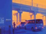 Silhouetted vehicles and person under an elevated highway overpass at dusk, with warm artificial lighting illuminating the concrete infrastructure against a deep blue sky, depicting an urban transportation scene.