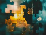 Abstract illustration of interlocking puzzle pieces in warm and cool tones against a blurred, colorful background, symbolizing the concept of problem-solving or finding solutions through collaboration and combining different elements.