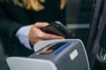 Close-up view of a person’s hands using a smartphone to make a contactless payment by tapping it on a point-of-sale terminal, illustrating mobile payment technology and digital transactions.