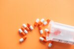 Scattered orange and white capsules arranged to spell “HELP” on an orange background, symbolizing a cry for medical assistance or the concept of drug addiction and dependence.