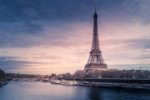 The iconic Eiffel Tower in Paris stands tall against a colorful sunset sky, with the Seine River and boats visible in the foreground, creating a picturesque and recognizable scene of one of the world’s most famous landmarks.