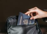 Close-up view of a hand holding a United States passport, partially inserted into an open zipper compartment of a bag, depicting the concept of international travel and border security.