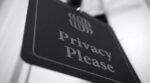 Close-up photograph of a black and white sign or placard with the text “Privacy Please” engraved on it, highlighting the concept of privacy and personal boundaries.