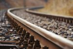 Close-up view of curved railroad tracks laid on gravel, with the rails and ties in sharp focus against a blurred background, depicting transportation infrastructure and the concept of journey or travel.