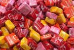 Pile of unwrapped, crumpled candy wrappers in shades of red, pink, orange, and yellow, depicting the excessive waste and environmental impact of single-use plastic packaging for confectionery products.